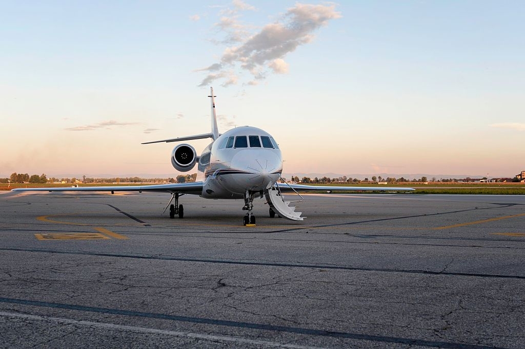 Front view of private jet parked on airport runway during the sun set, dusk. Open vehicle door, ready to boarding passenger.